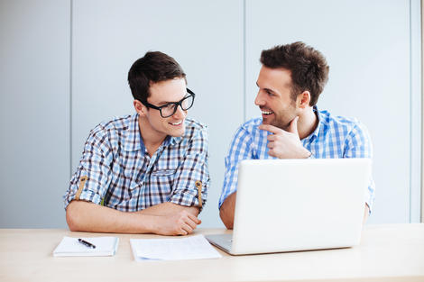 two male colleagues chatting in office in front of laptops